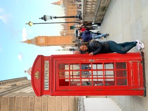 solo female traveler standing in front of a read phone booth, in London, with Big Ben in the background during a solo London trip