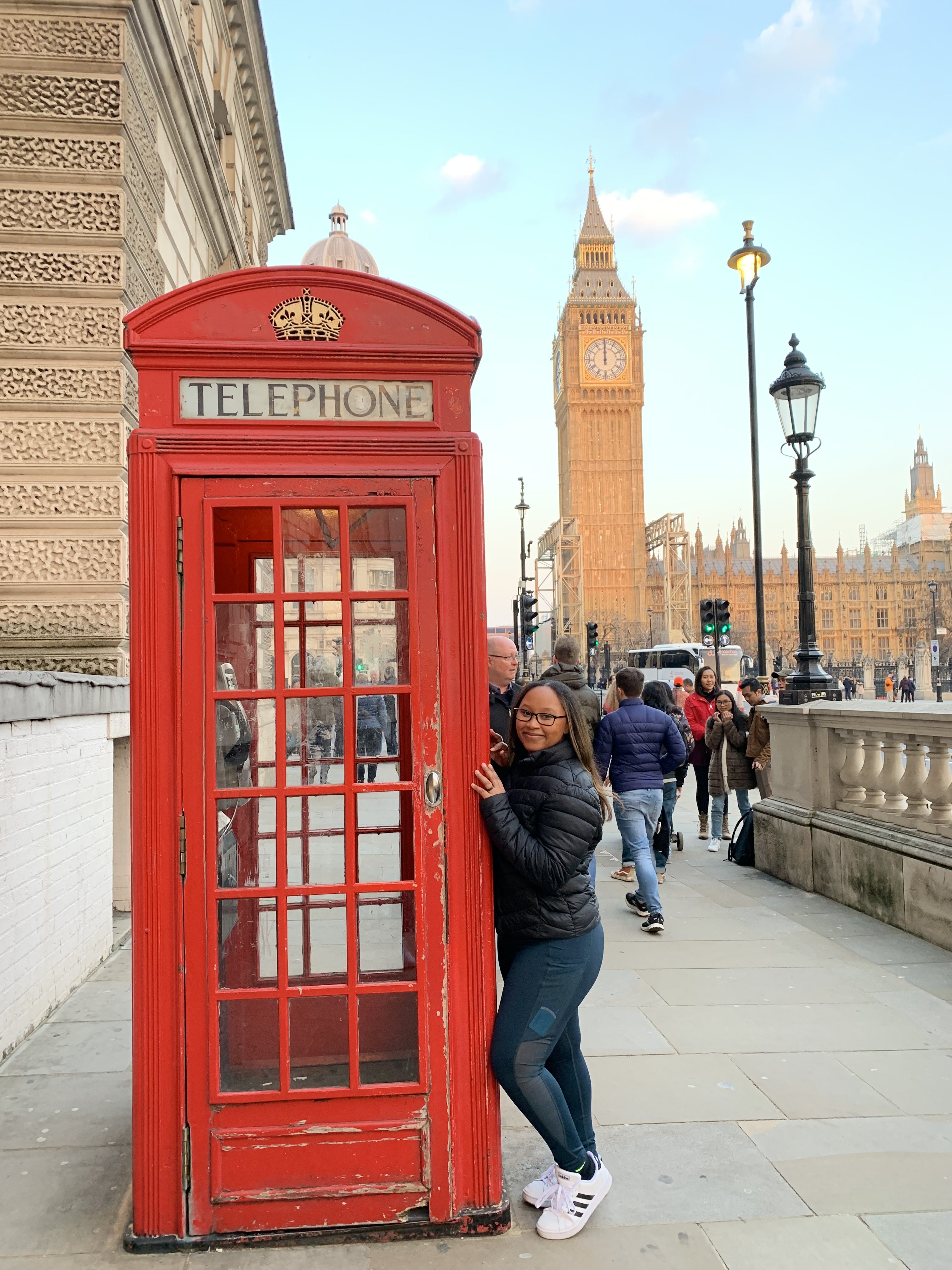 solo female traveler standing in front of a read phone booth, in London, with Big Ben in the background during a solo London trip